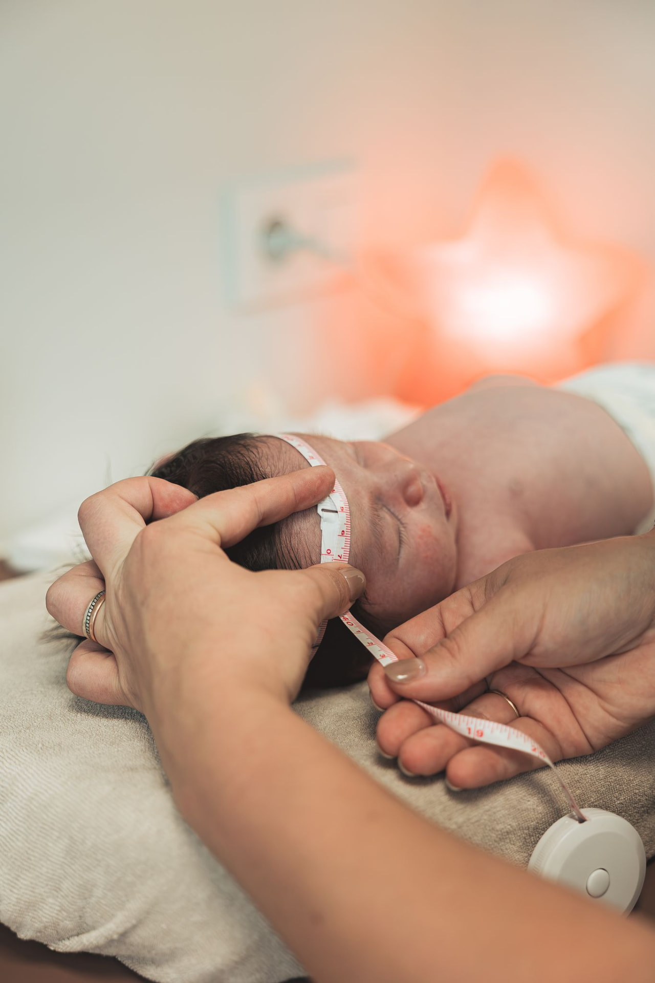 Vroedvrouw meet zachtjes de hoofdomtrek van een slapend pasgeboren baby